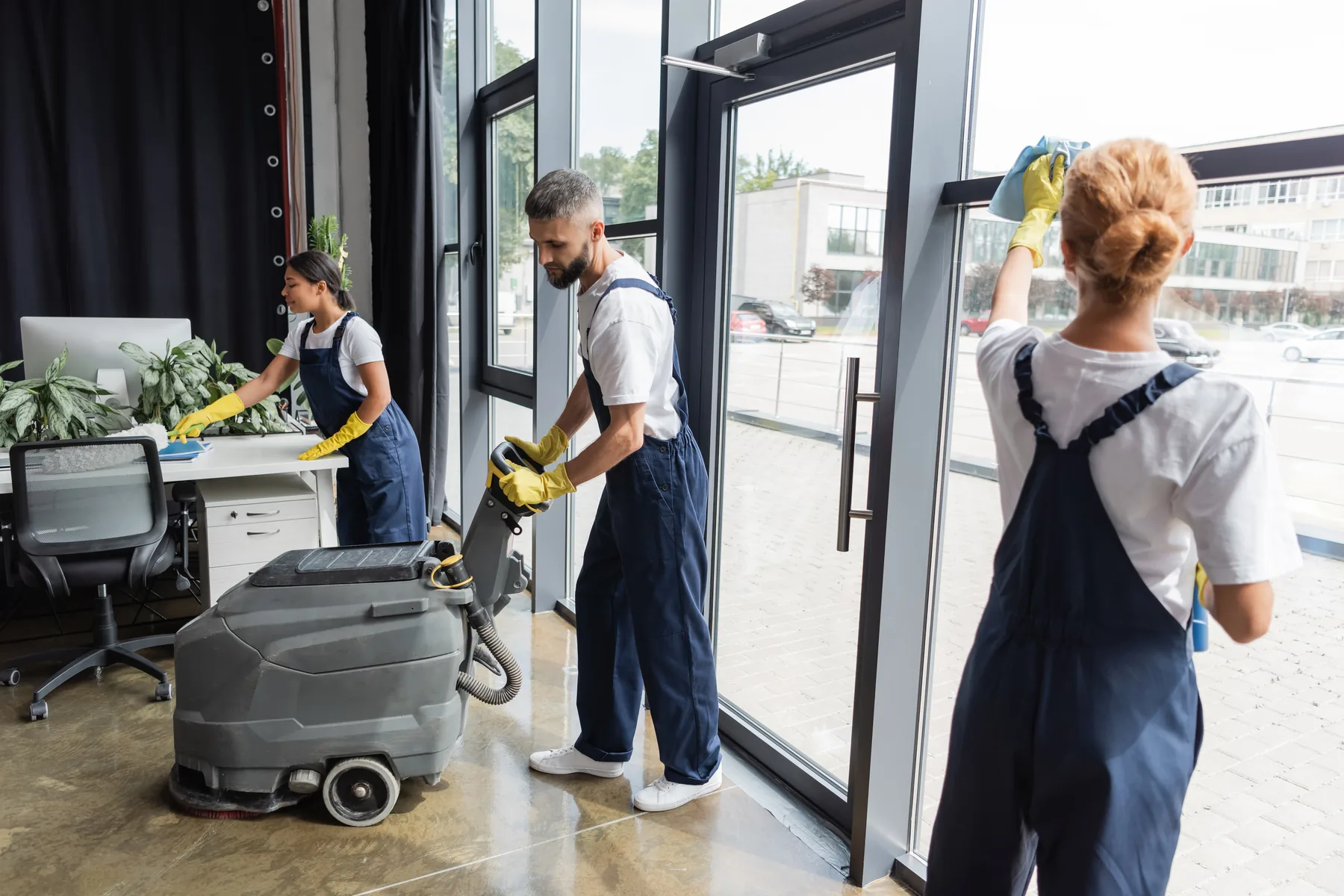 A cleaning crew at work in an office, one operating a floor scrubber