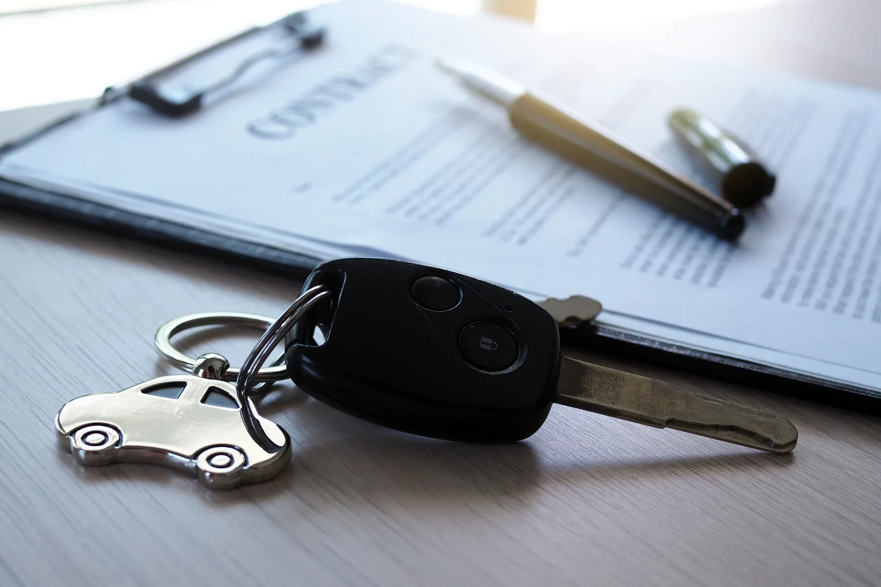 A car key resting on a printed contract next to a pen