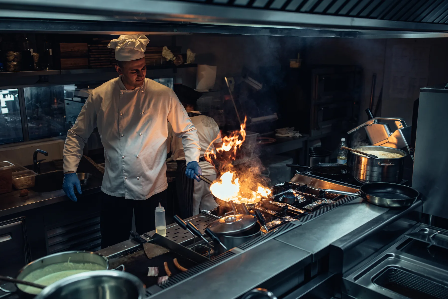 A chef working at a lit commercial range in a professional kitchen